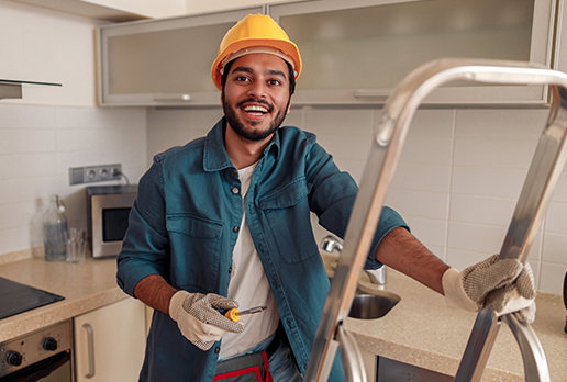 Maintenance man smiling at work on ladder in a kitchen